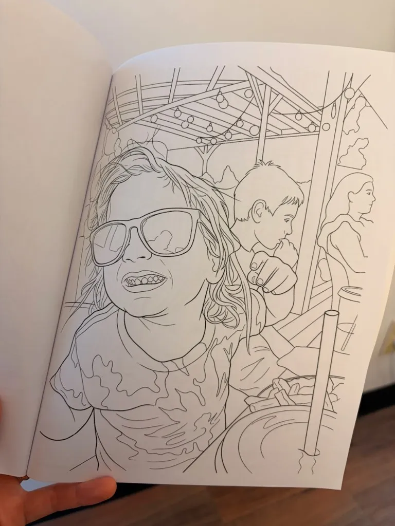 Photograph of an open Robertson Family Summer book showing a printed coloring page of children at a patio dinner
